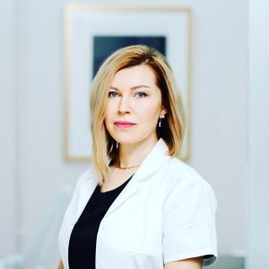 Medicīnas zinātņu doktore Māra Rone-Kupfere baltā ārstes halātā, skatās kamerā – ādas veselības eksperte Latvijā.