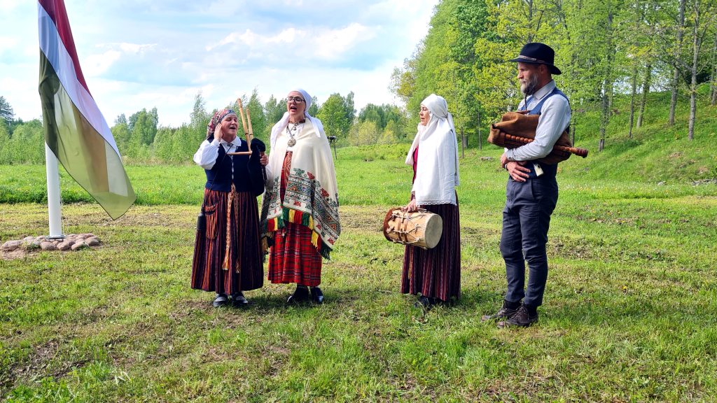 Sēļu tradicionālās mūzikas grupa "Krāce" tautastērpos ar mūzikas instrumentiem pie Sēlijas karoga masta Sunākstē.
