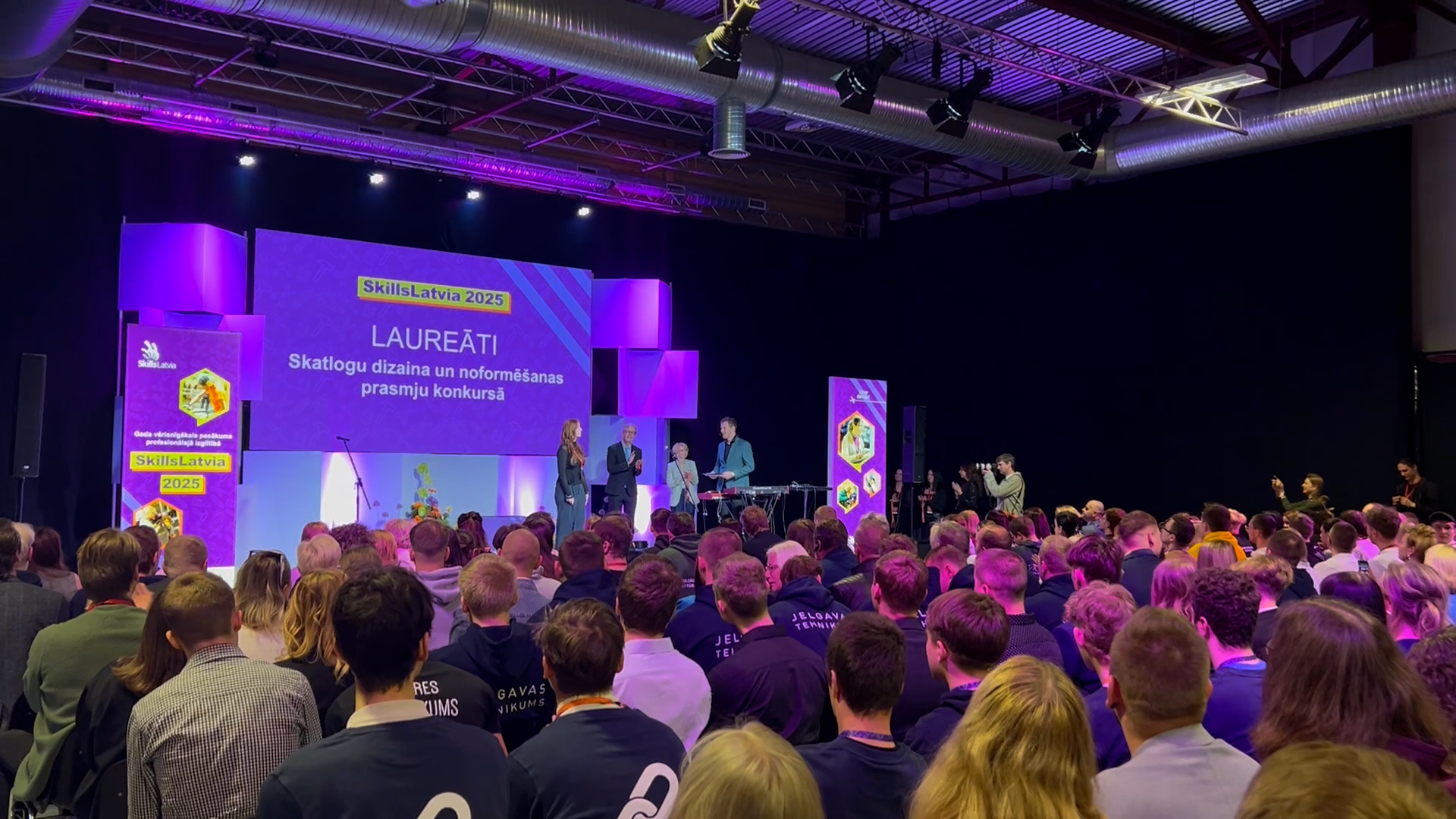 Skatītāju pilna zāle klausās "SkillsLatvia 2025" laureātu paziņošanas ceremoniju skatuves priekšā.