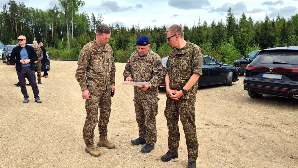 Valsts prezidents Edgars Rinkēvičs un militārpersonas sarunājas un aplūko dokumentus Sēlijas militārajā poligonā