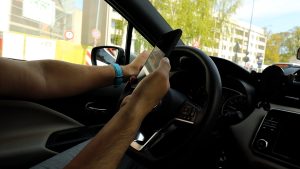 Vadītājs automašīnā lieto mobilo telefonu pie stūres