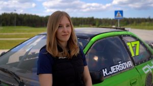 Autosportiste Kitija Jeršova stāv pie sava zaļā sacīkšu auto ar numuru 17