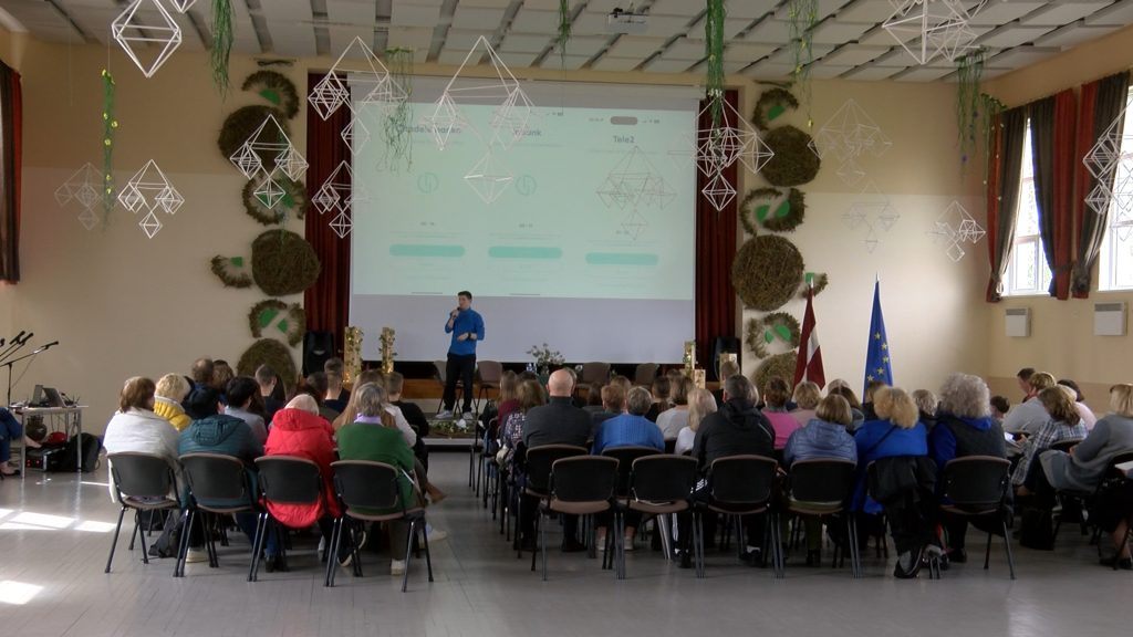 Lektors stāv pie tribīnes un runā auditorijas priekšā par drošības tēmām