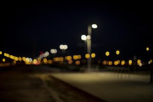 Izpludinātas pilsētas gaismas naktī ar ielu apgaismojuma spuldzēm priekšplānā