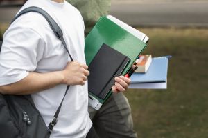Studenti ar mapēm, piezīmēm un mugursomām brīvā dabā