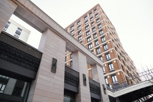 Mūsdienīga daudzdzīvokļu māja ar kārniņu jumtu un gaišas krāsas fasādes elementiem