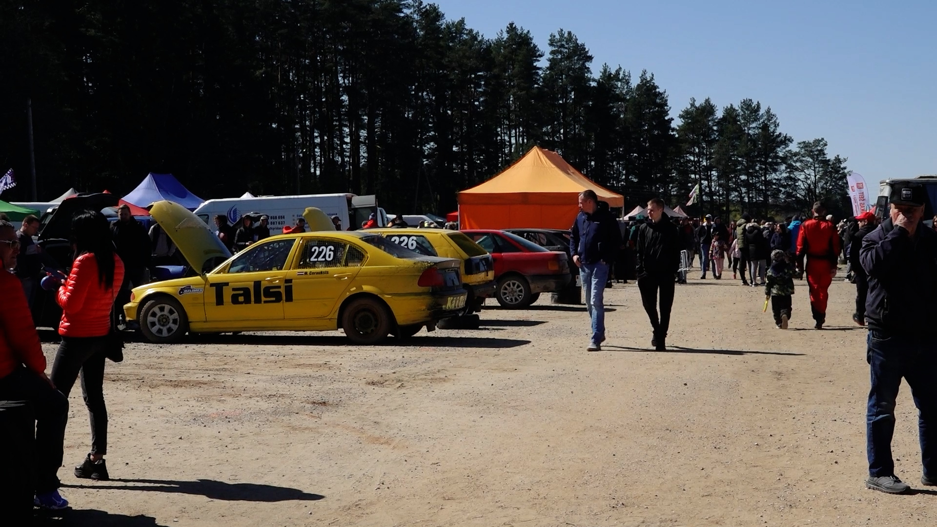 Folkreisa auto sacensību dalībnieku parks Smiltenē, redzami dažādi auto un cilvēki.