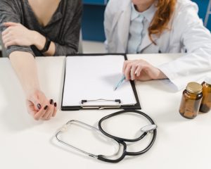 Ārsts konsultē pacientu, galdā stetoskops un dokumenti