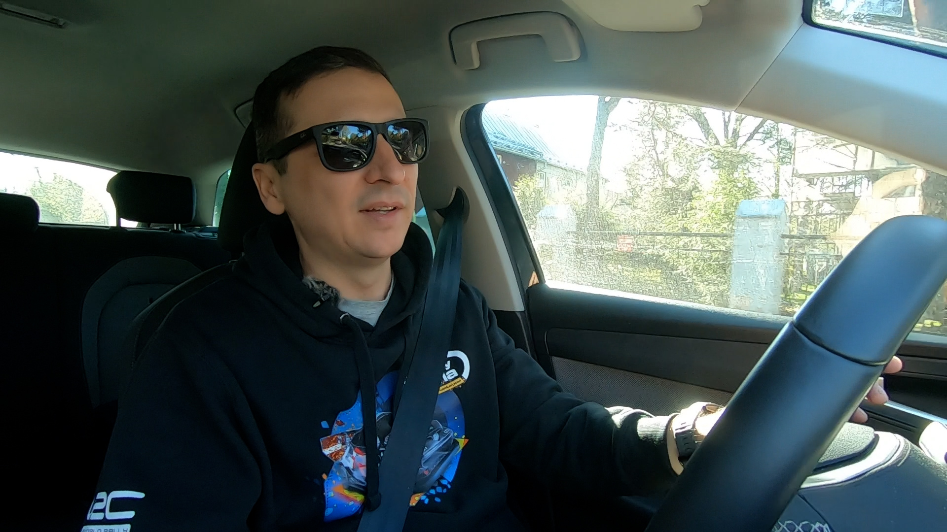 Raimonds Strokšs automašīnā, valkājot WRC sporta džemperi un saulesbrilles