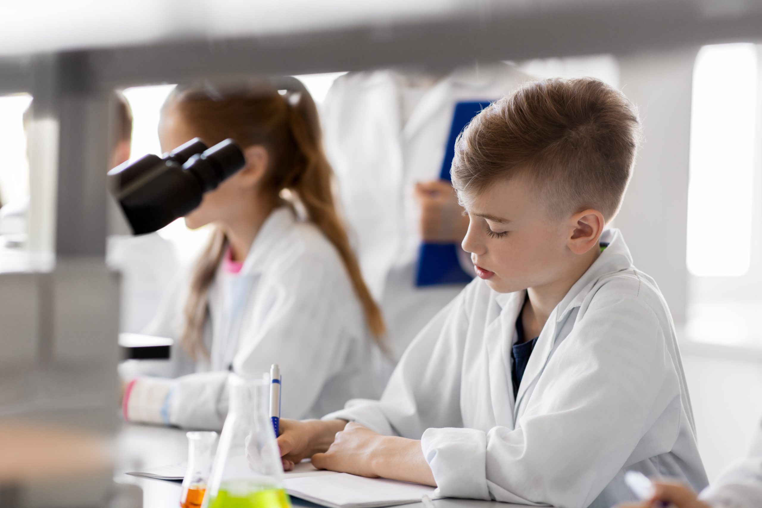 Skolēni baltos halātos mācās ķīmiju laboratorijā