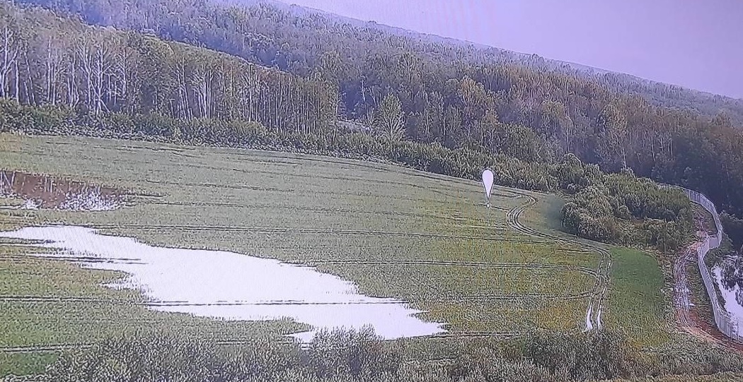 Lauks ar ūdens peļķēm un baltu meteoroloģisko zondi attālumā, ar mežu fonā