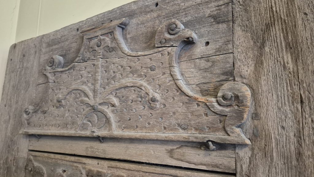Senas koka durvis ar grebtiem ornamentiem un metāla detaļām tuvplānā