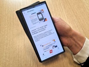 Persona tur viedtālruni, kurā redzama Valsts ugunsdzēsības un glābšanas dienesta (VUGD) lietotnes "112 Latvija" sadaļa "Aktualitātes" ar informāciju par pieejamo informāciju par patvērumiem.