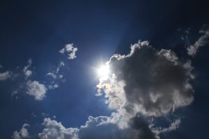 Saule spīd caur mākoņiem zilajās debesīs