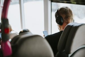 Vīrietis ar austiņām klausās mūziku autobusā, skatoties telefonā