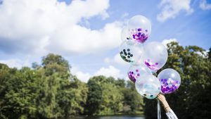 Roka tur caurspīdīgus balonus ar krāsainu konfeti pie upes svētku noskaņā