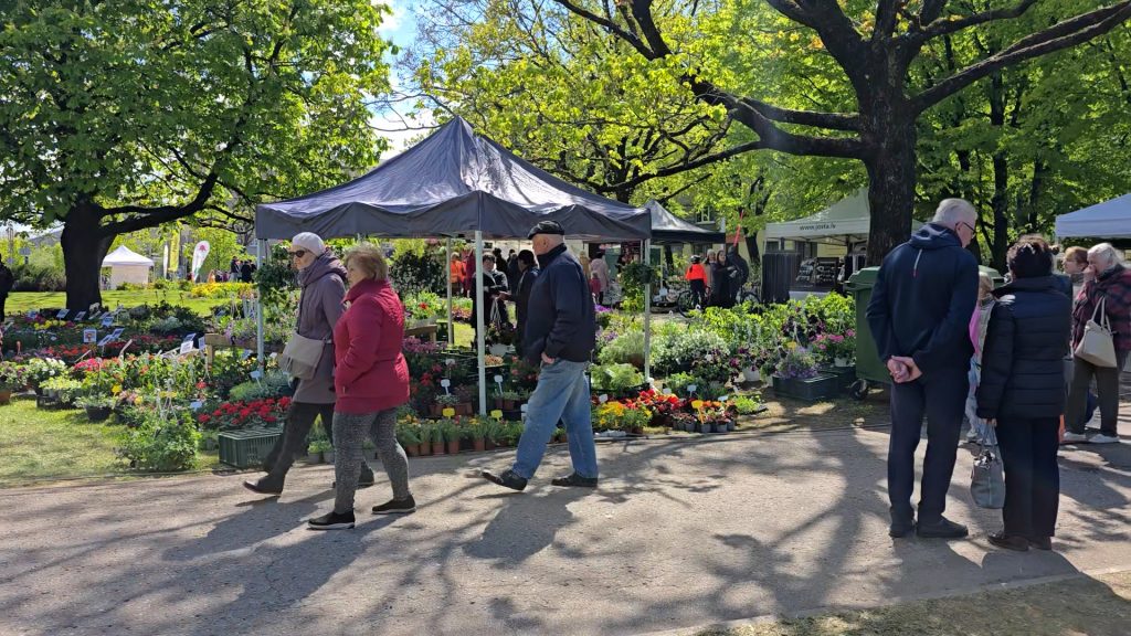 Cilvēki pastaigājas gar stendiem ar stādiem un kokiem stādu tirdziņā parkā