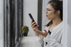 Sieviete ar brillēm runā pa telefonu ar satrauktu vai neizpratnes pilnu sejas izteiksmi.