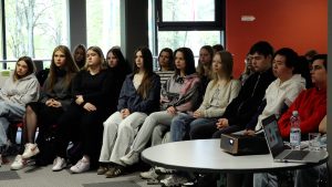 Vidusskolēni sēž zālē un klausās lekciju vai diskusiju