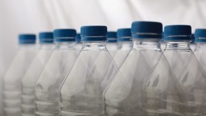 Tukšas plastmasas PET pudeles ar ziliem korķiem, kas stāv rindā