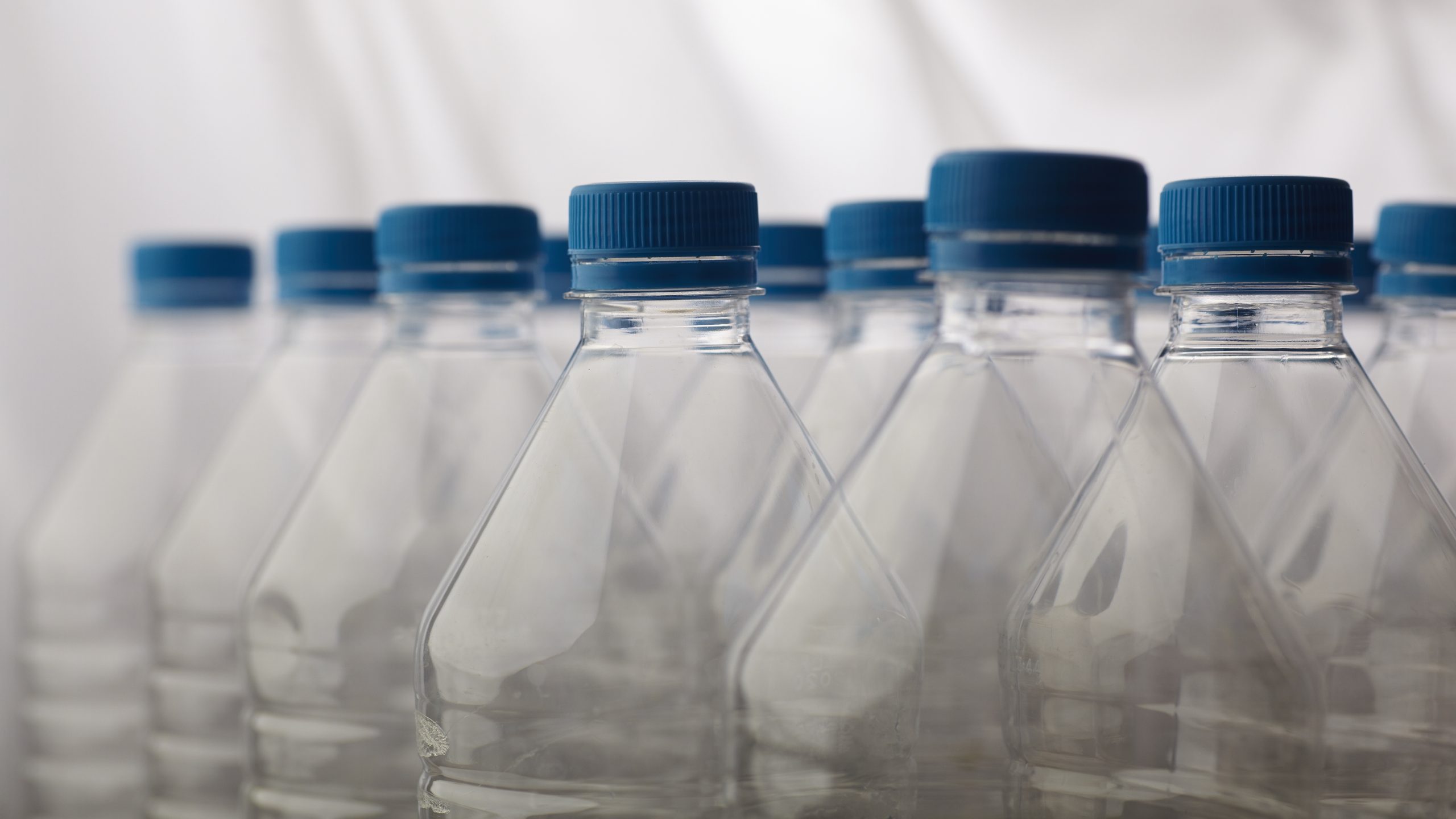 Tukšas plastmasas PET pudeles ar ziliem korķiem, kas stāv rindā