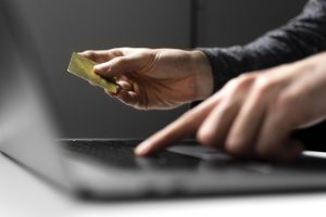Persona tur zelta kredītkarti, ar otru roku rakstot uz klēpjdatora tastatūras