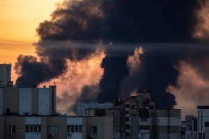 Pilsētas apbūve ar milzīgu dūmu mākoni un liesmām fonā