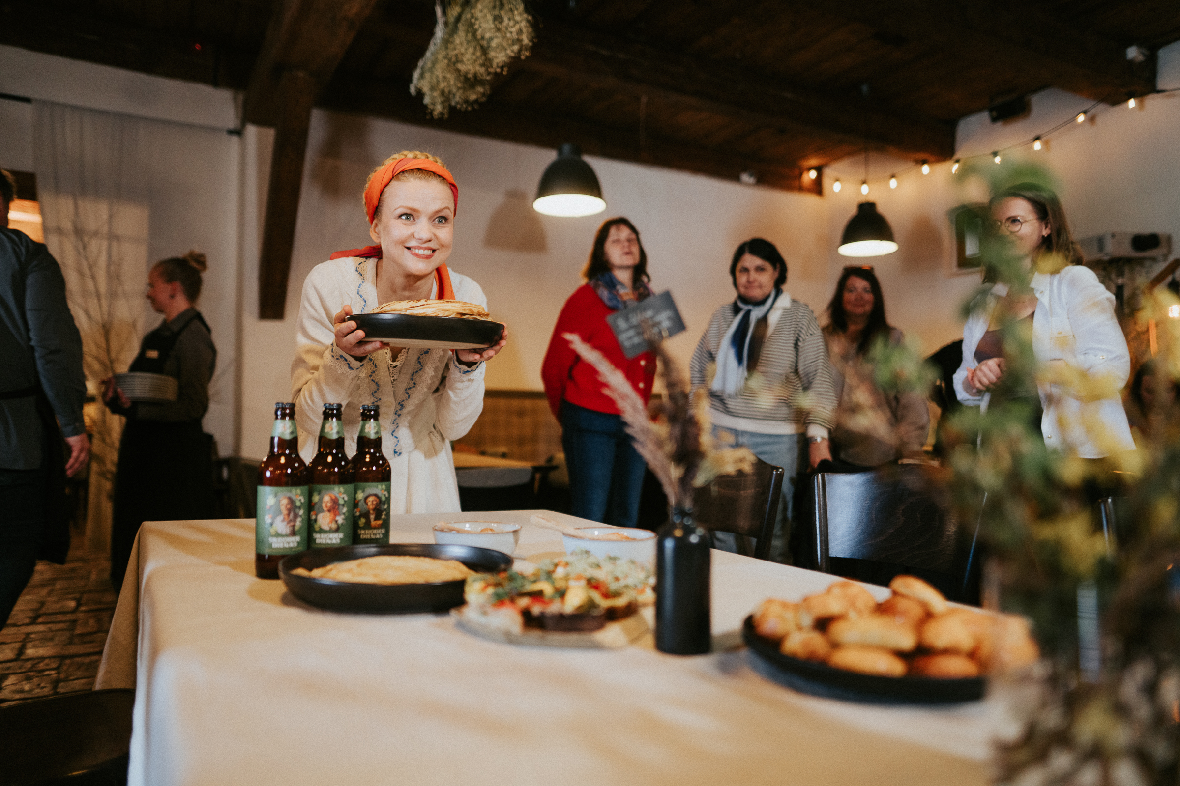 Sieviete tautiskā tērpā pasniedz pīrāgu Valmiermuižas alus degustācijā