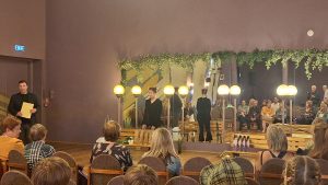 Pasākuma zāle ar skatītājiem, spoguļiem un cilvēkiem uzstājoties