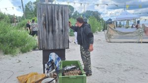 Vīrietis kūpina zivis pludmalē Zivju dienas pasākumā Kaugurciemā.
