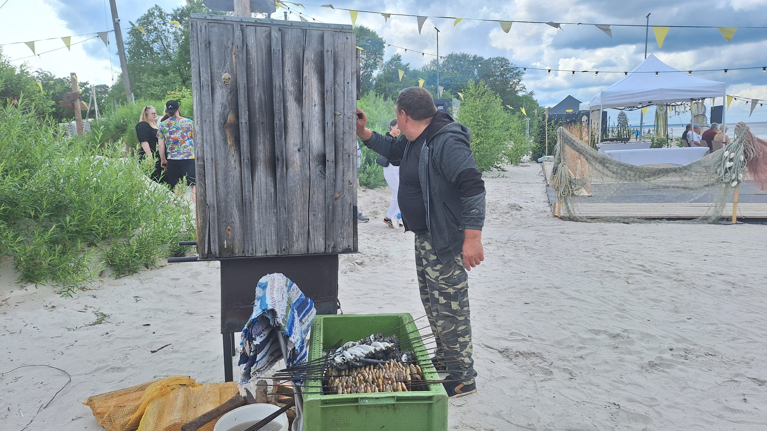 Vīrietis kūpina zivis pludmalē Zivju dienas pasākumā Kaugurciemā.