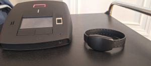 Elektroniskās uzraudzības aproce un bāzes stacija uz galda.