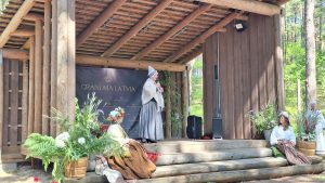 Sieviete tautastērpā uzstājas uz skatuves pasākumā “Grandma Latvia”