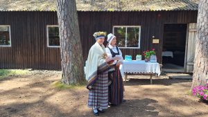 Divas sievietes tautastērpos pie lauku muzeja ēkas pasākuma laikā