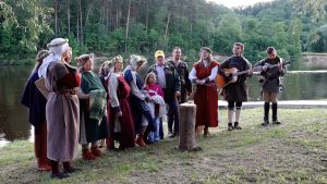 Folkloras kopa tautastērpos dzied pie upes