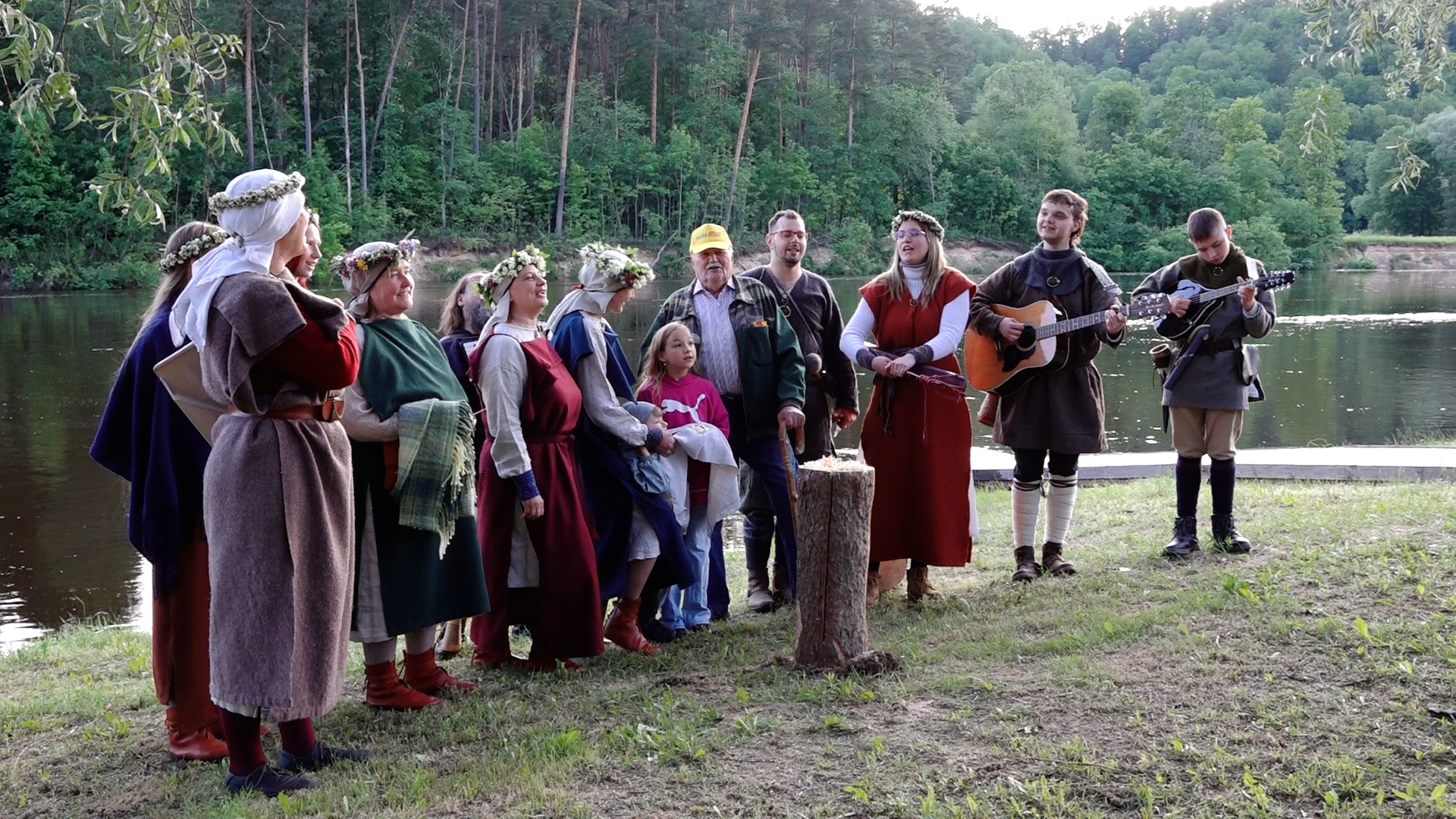 Folkloras kopa tautastērpos dzied pie upes