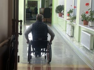 Vīrietis ratiņkrēslā pārvietojas pa aprūpes centra gaiteni