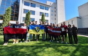 Grupas foto ar Latvijas un Ukrainas karogiem pie ēkas Ukrainā