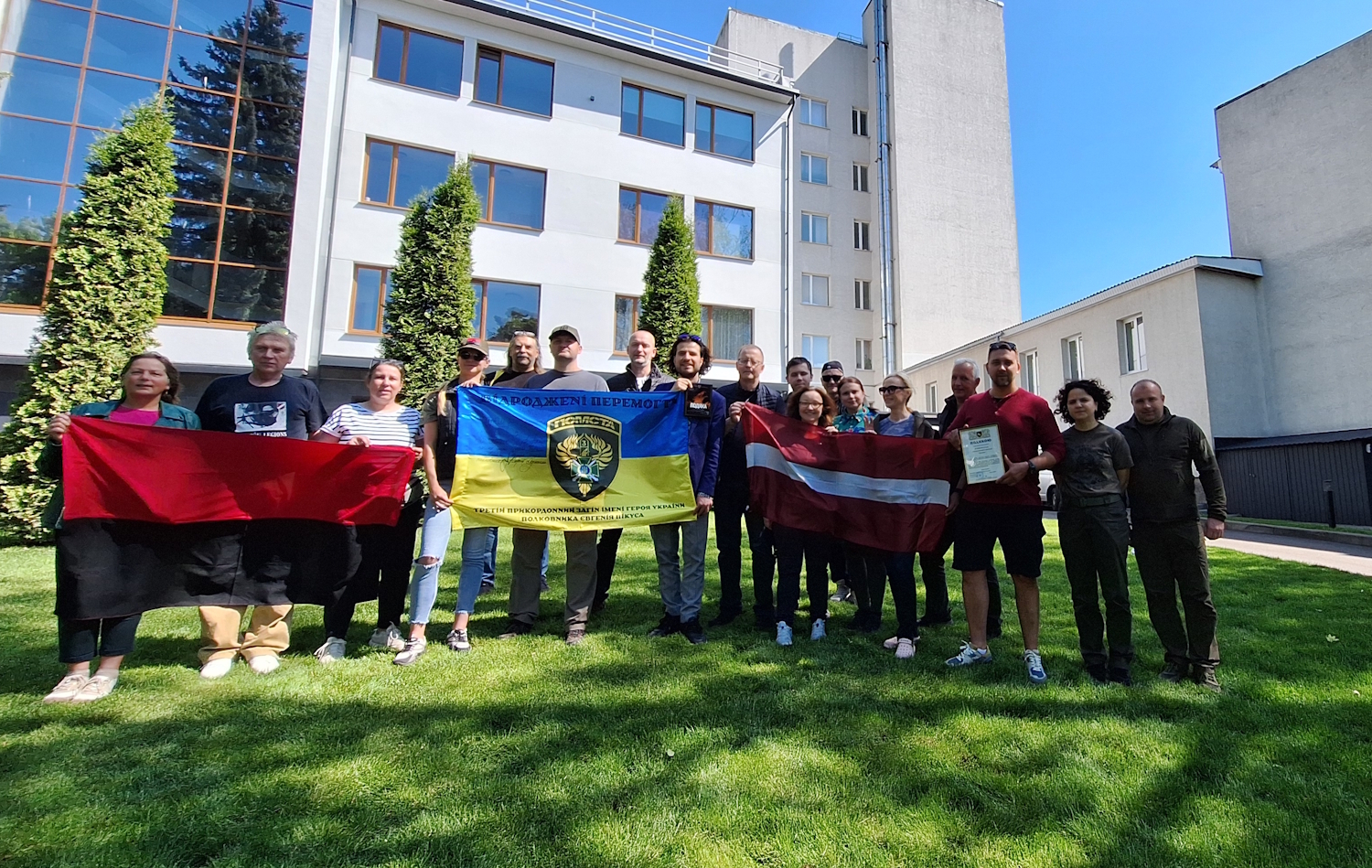 Grupas foto ar Latvijas un Ukrainas karogiem pie ēkas Ukrainā