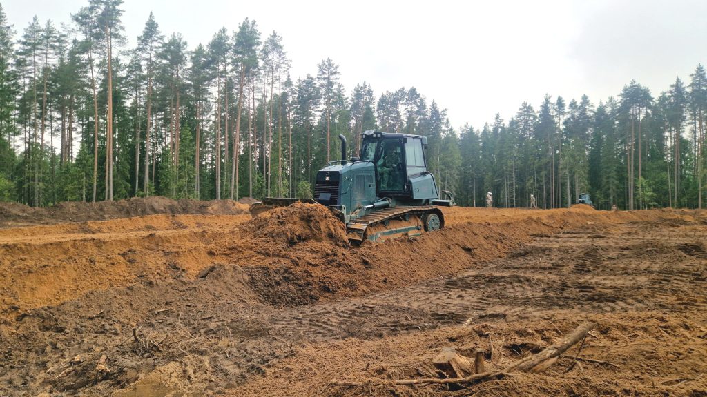 Buldozers veic zemes rakšanas darbus Sēlijas militārajā poligonā, stumjot lielu zemes kaudzi