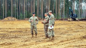 Trīs ASV militārpersonas militārajās uniformās sarunājas Sēlijas militārā poligona būvlaukumā