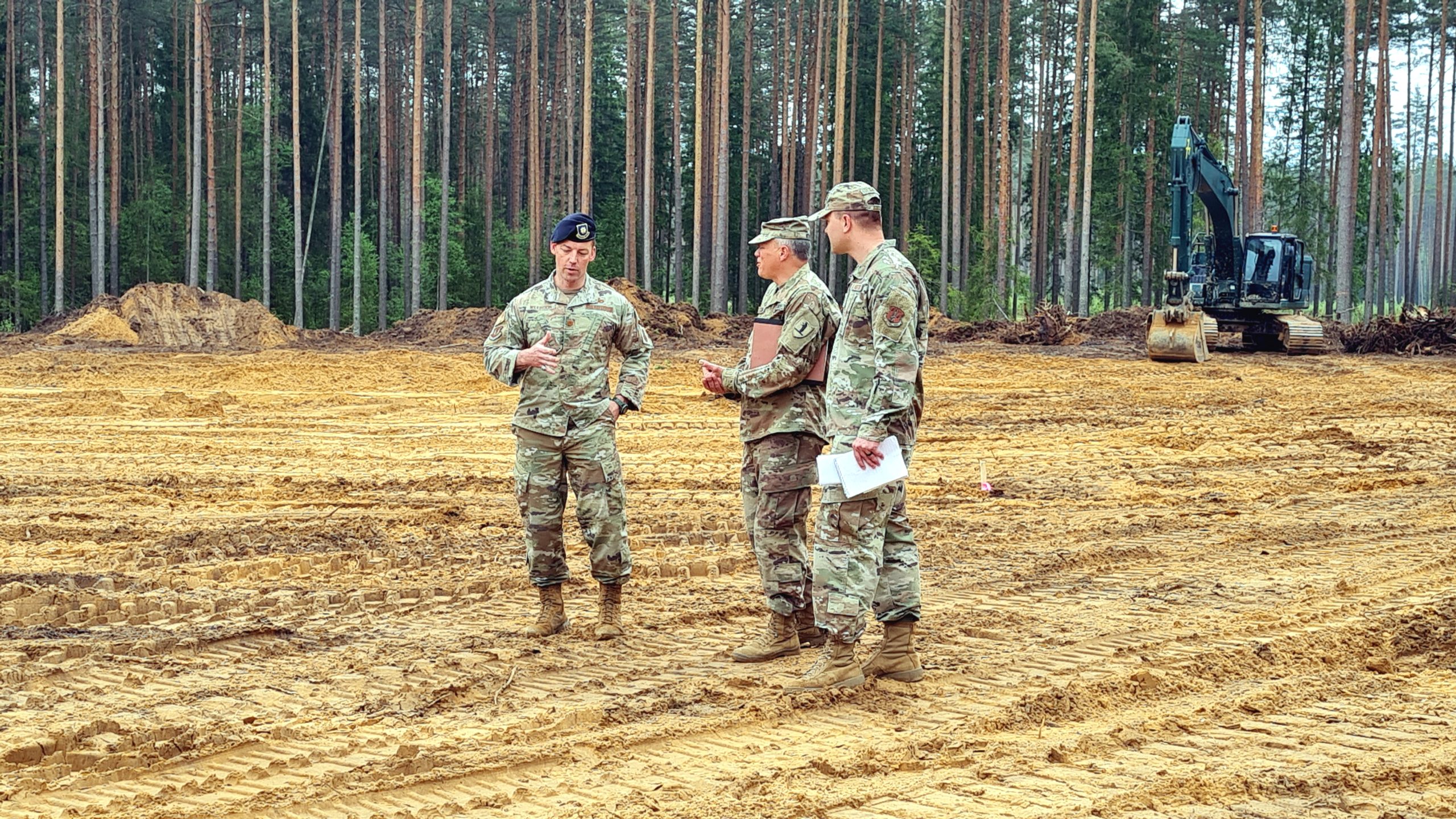 Trīs ASV militārpersonas militārajās uniformās sarunājas Sēlijas militārā poligona būvlaukumā