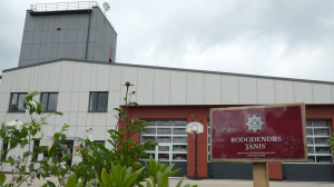 Ugunsdzēsēju depo ēka ar zīmi "RODODENDRS "JĀNIS"" priekšplānā un basketbola grozu.