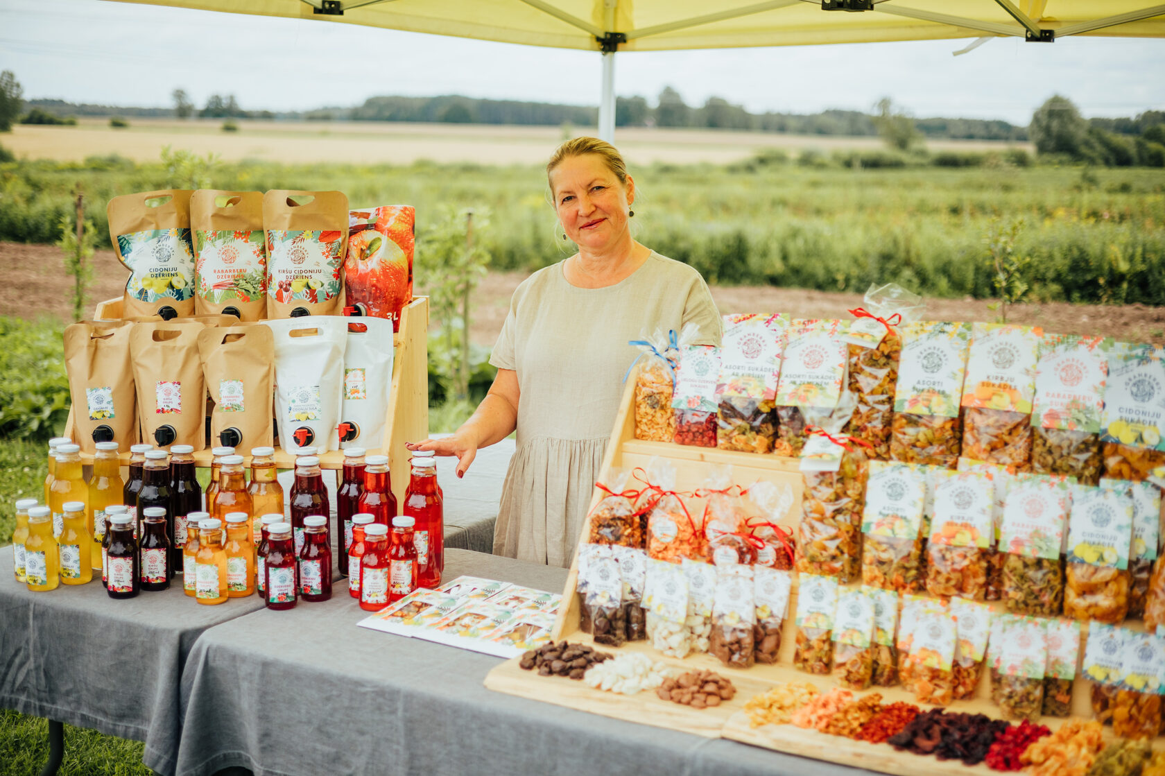 Sieviete lauku tirdziņā piedāvā cidoniju dzērienus un kaltētus augļus vietējo produktu stendā