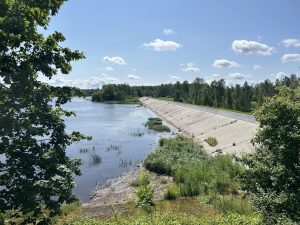 Panorāmas skats uz Daugavu ar zaļu veģetāciju un betona konstrukciju gar krastu