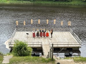 Tuvplāns ar sieviešu vokālo ansambli tautas tērpos uz peldošās skatuves uz Ogres upes