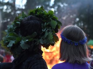 Līgotāji ar vainagiem skatās uz ugunskuru Jāņu naktī.