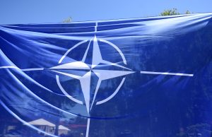 NATO karogs vējā ar atspulgiem fonā