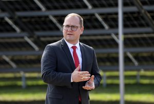 Raimonds Čudars ar sarkanu kaklasaiti runā pie saules paneļiem