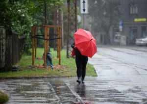 Cilvēks lietū ar sarkanu lietussargu uz pilsētas ietves